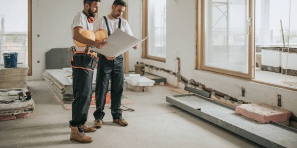 Young manual workers standing at construction site and examining blueprints.