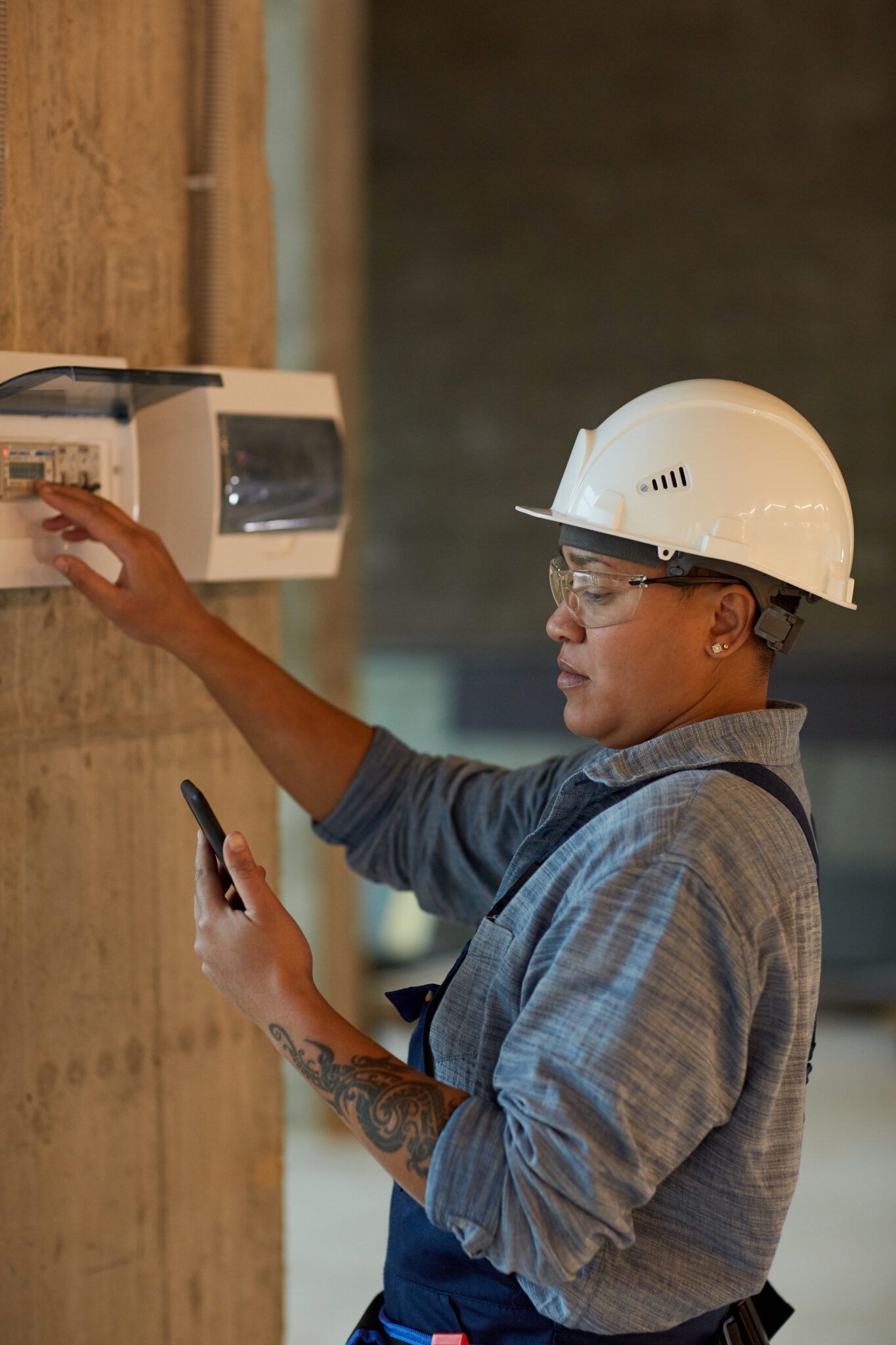 Vertical side view portrait of female worker setting up electricity and using smartphone while working on construction site